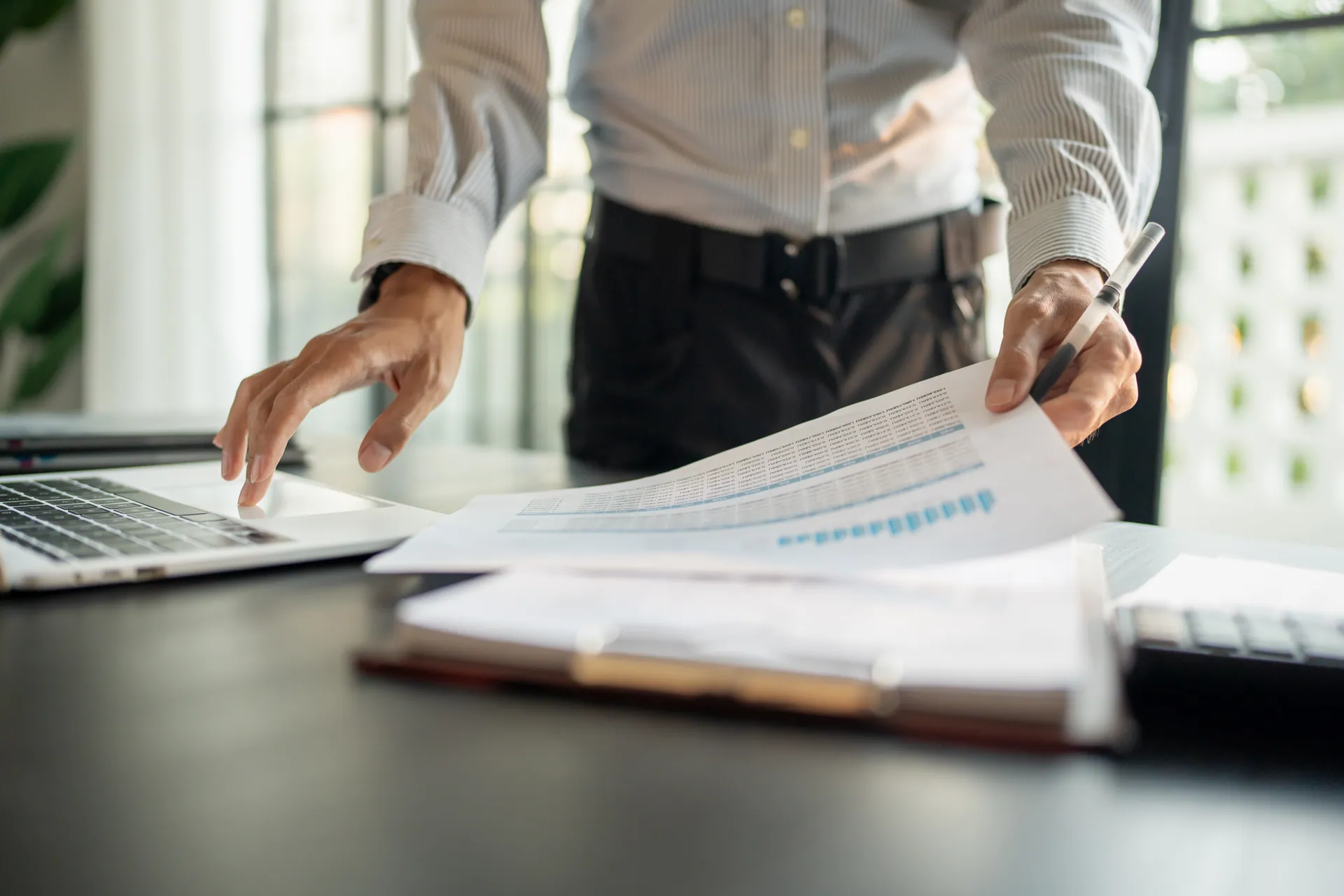 Professional reviewing a financial report with a pen beside a laptop